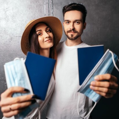 smiling-couple-standing-hold-passports-blue-face-disposable-medical-masks_267895-705